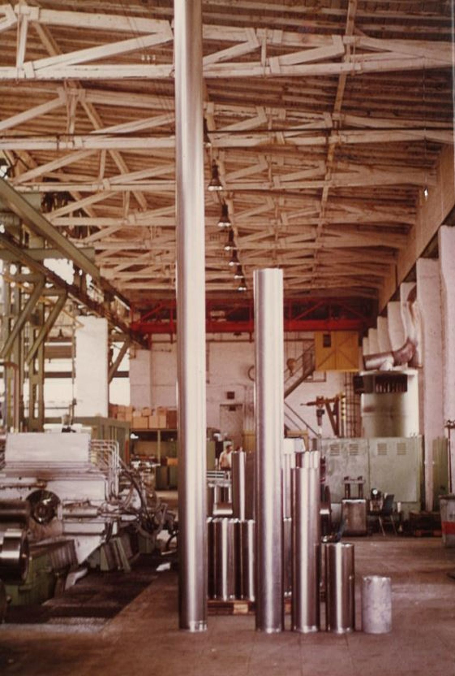 Industrielle Werkstatt mit hohen Metallzylindern, Maschinen und einer hohen Decke mit sichtbaren Balken. Geräte und Rohre sind überall im Raum sichtbar.