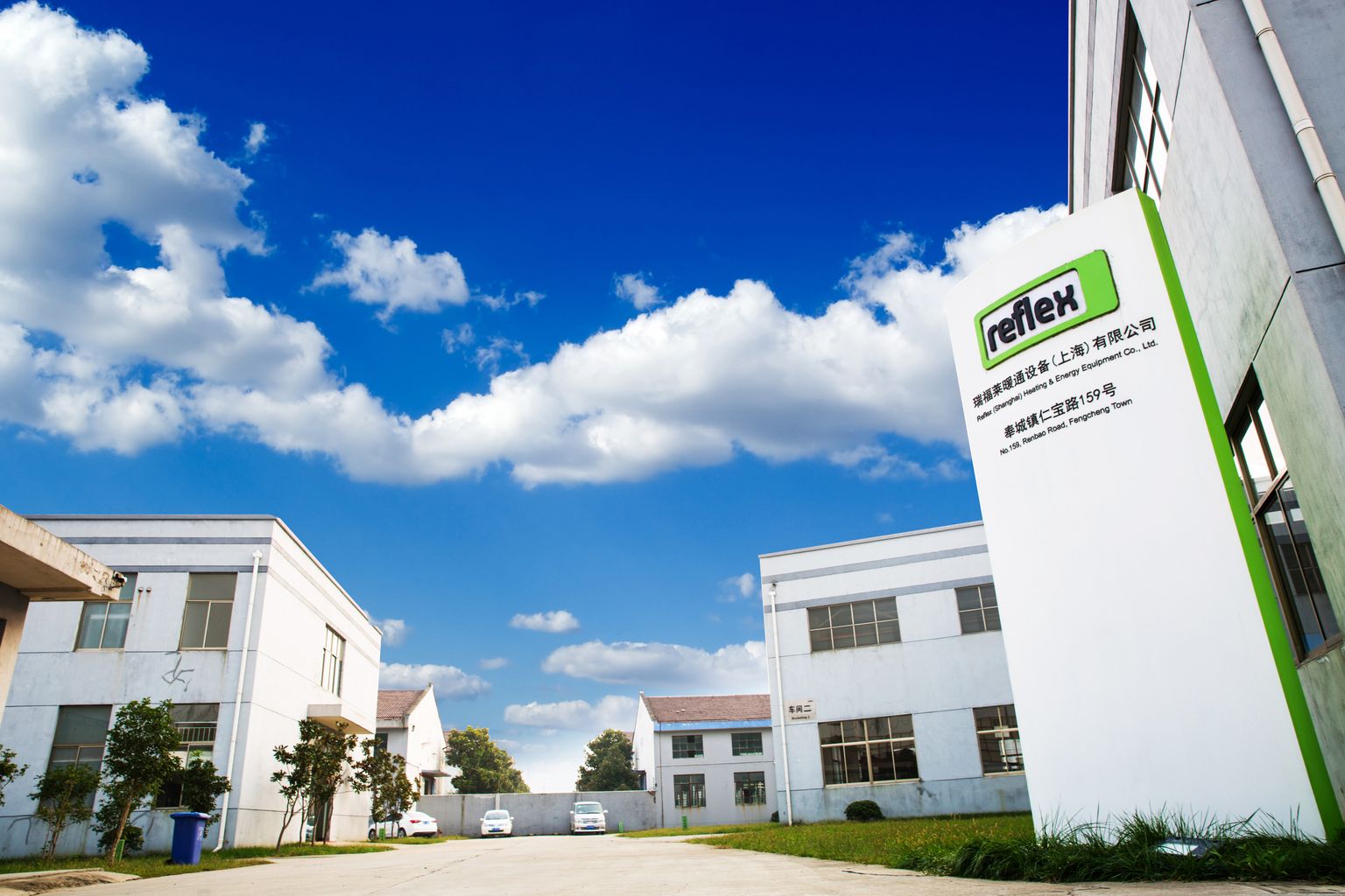 Moderne Industriegebäude mit einem großen Schild im Vordergrund, unter einem strahlend blauen Himmel mit vereinzelten Wolken.